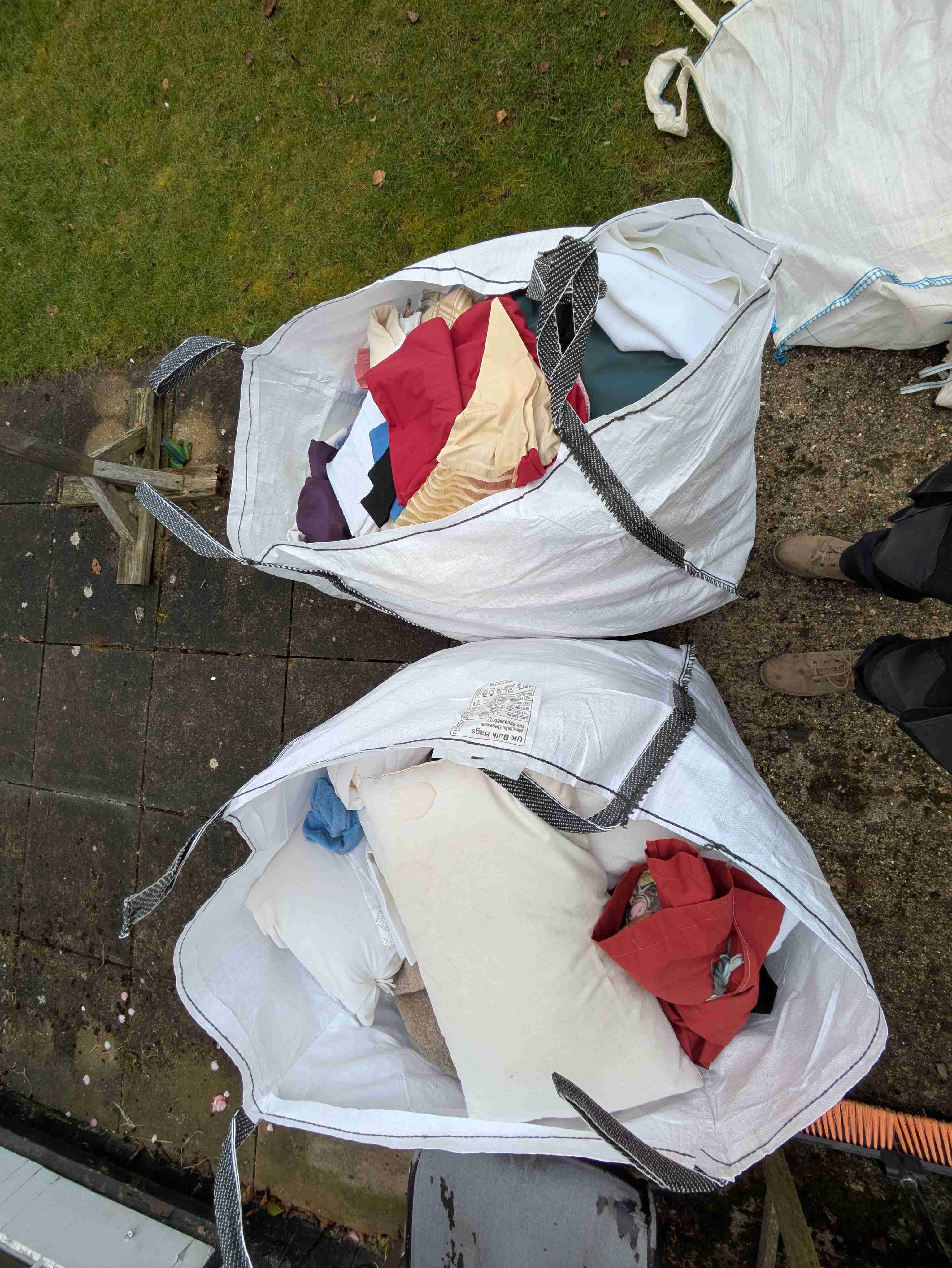 Two large white builders' bags filled with folded clothes and bedding ready for charity drop-off