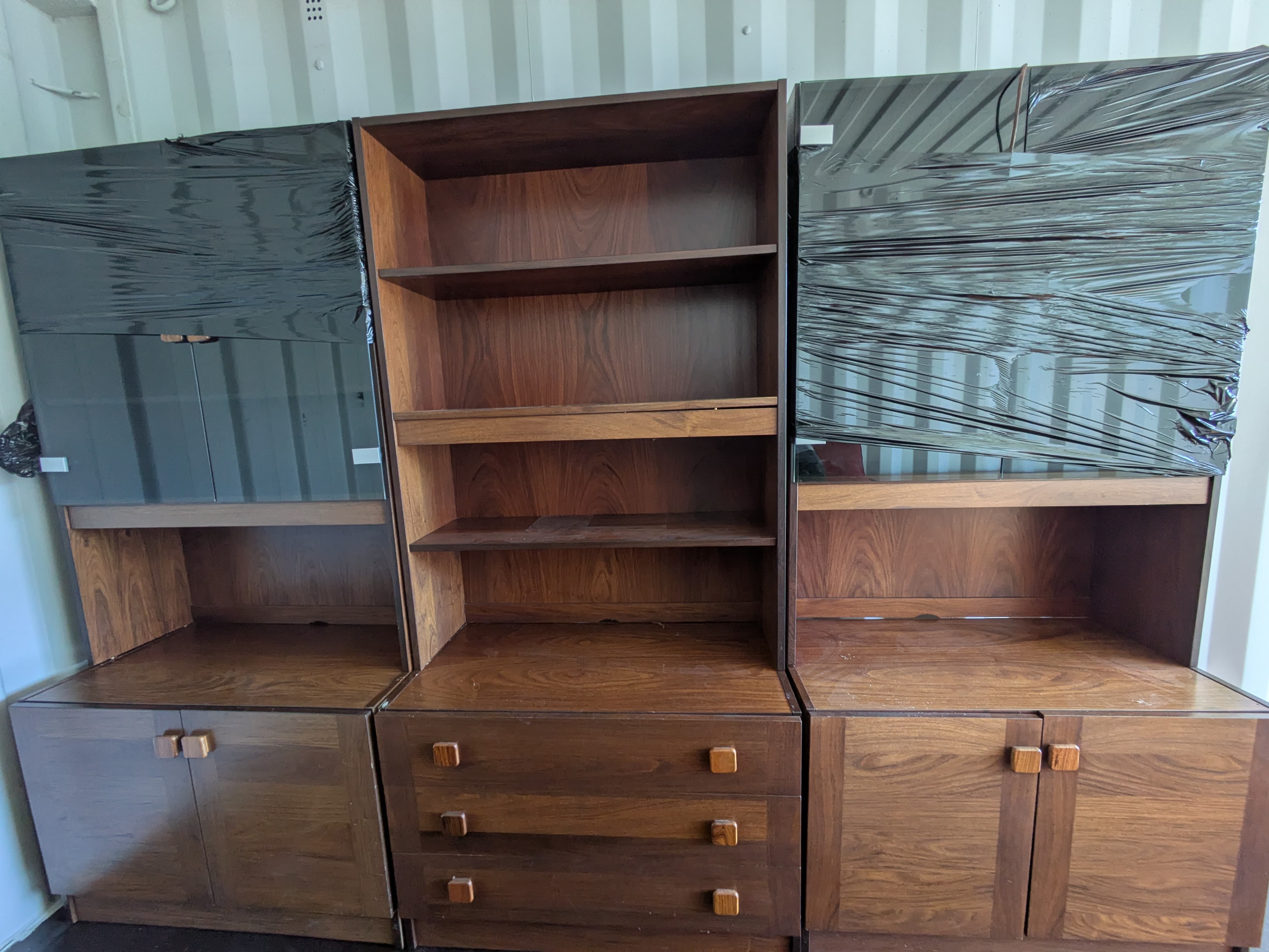 Three mid-century cabinets film-wrapped against scratches, lined up inside a self-storage container