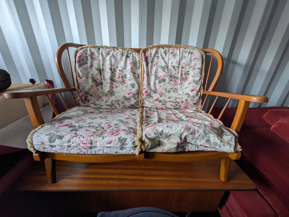 A wood-framed two-seater sofa with floral rose-print cushions, sat on top of a teak sideboard ready for collection